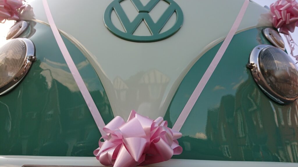 front of a splitscreen campervan with pink bow and ribbon